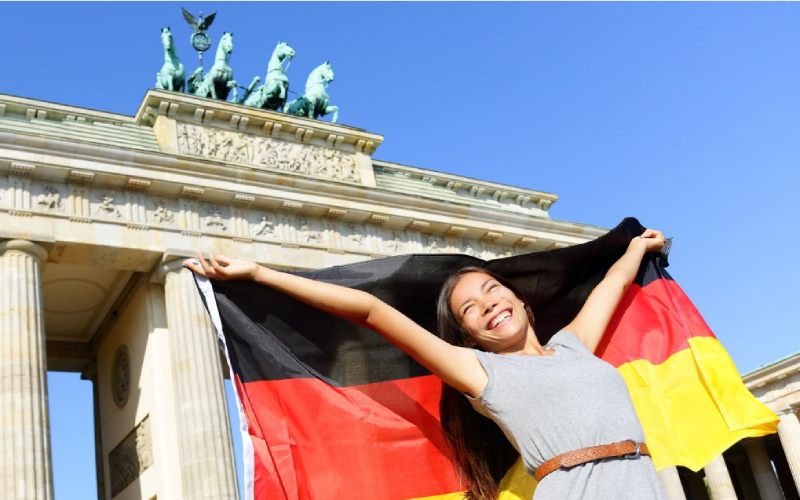 Une femme heureuse avec un drapeau allemand devant la porte de Brandebourg.