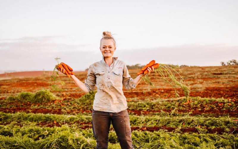 Une femme heureuse en Australie en train de récolter des carottes.